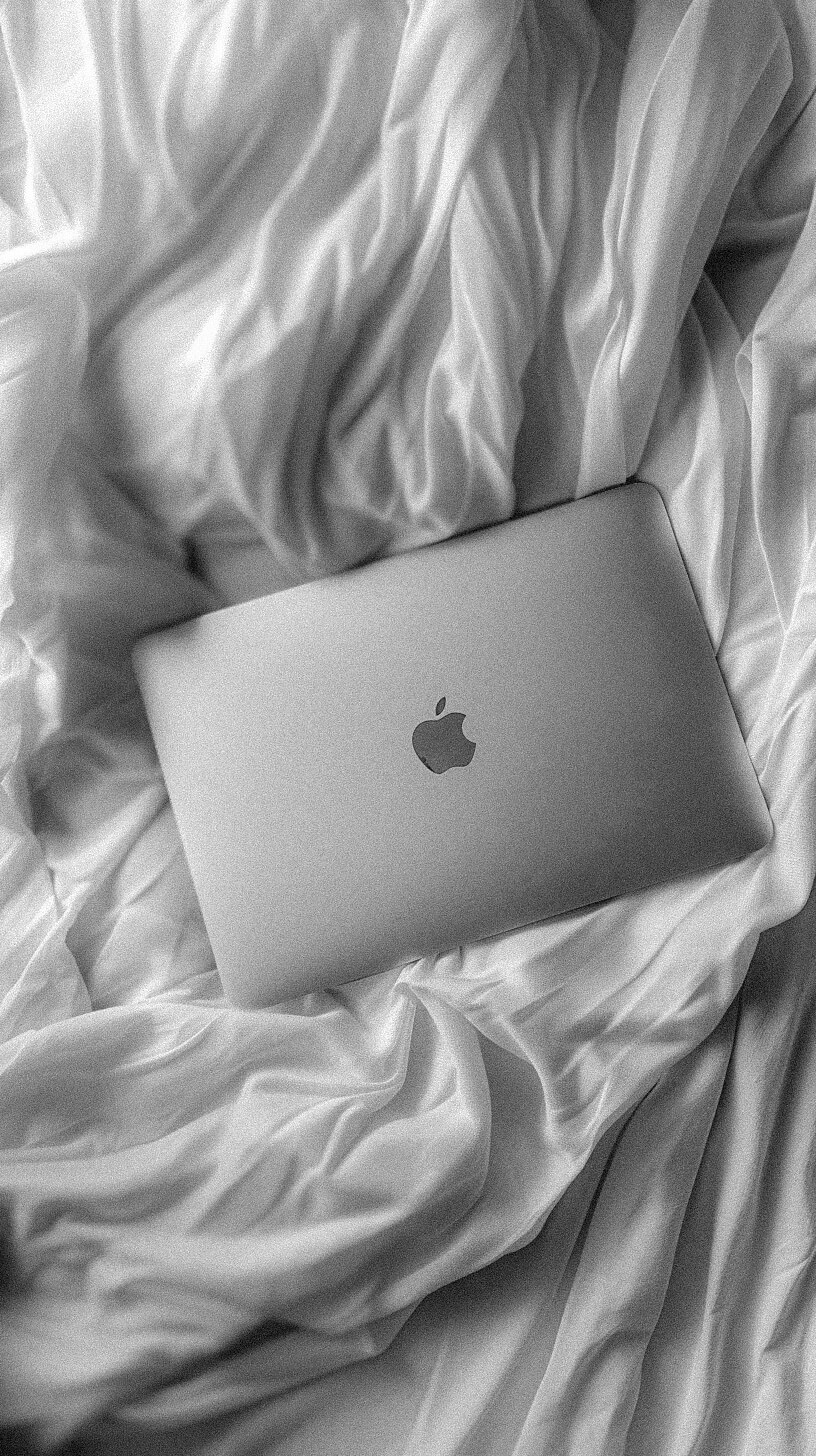 A closed laptop with an Apple logo rests on a bed with crumpled white sheets, its sleek design highlighted in black and white, much like the clean lines of a well-optimized Showit SEO layout.