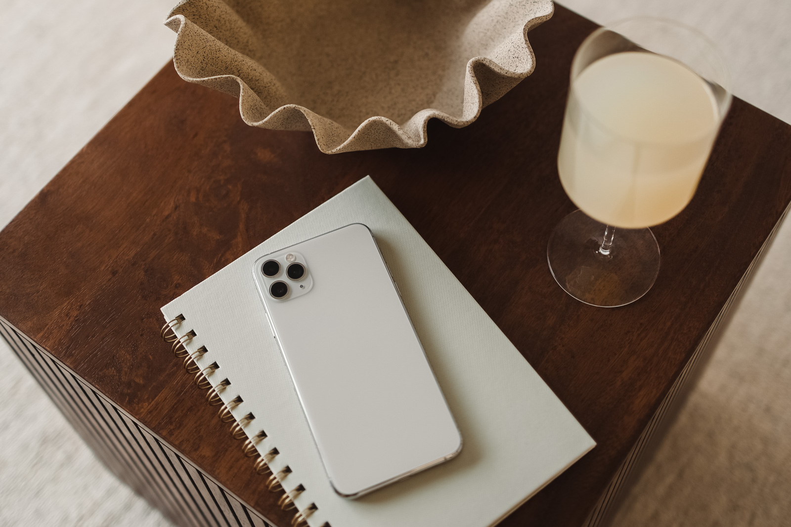iphone sitting on a side table with a notebook and a drink